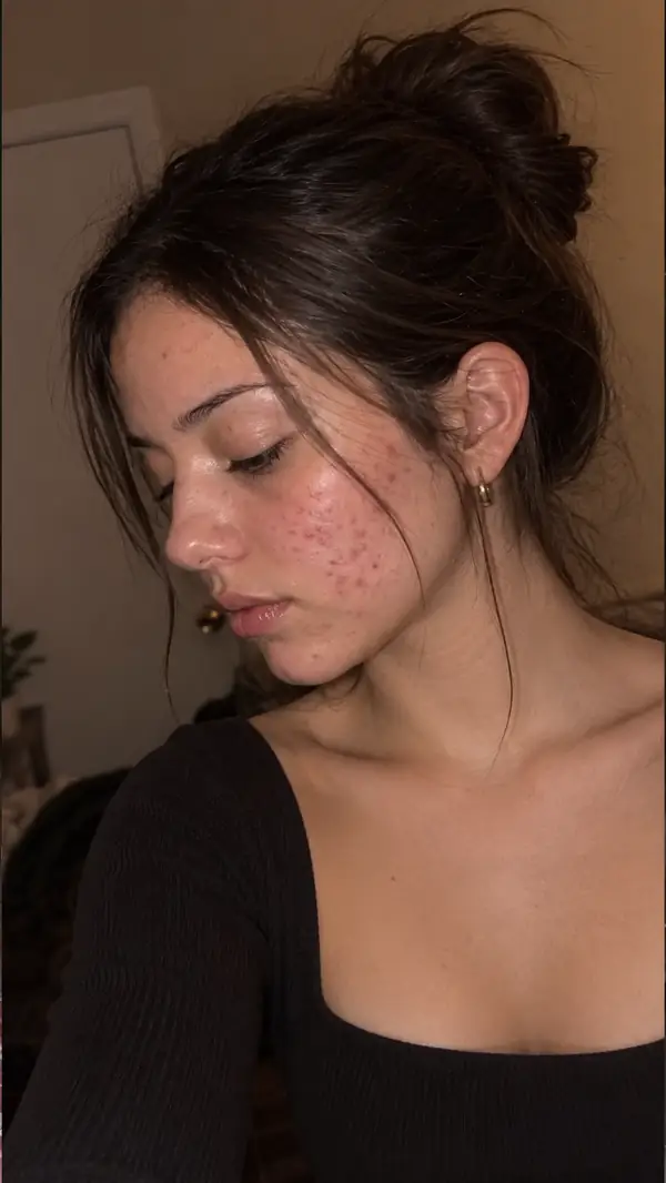 Ein Nahporträt einer jungen Frau in einem spontanen Beauty-Video-Moment, sanft beleuchtet.